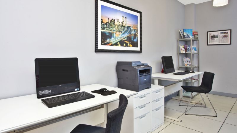 A business center with two white desks, two black chairs, a computer, a printer, and a filing cabinet.