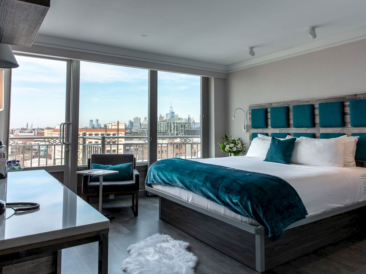 A modern hotel room with a large bed, desk, chair, and window offering a city view; features blue accents and sleek furnishings.