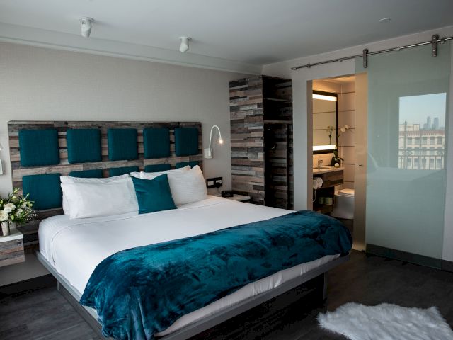 A wide view of a hotel room with a king-size bed, nightstand, and lamp, and a bathroom with shower and toilet in the background.