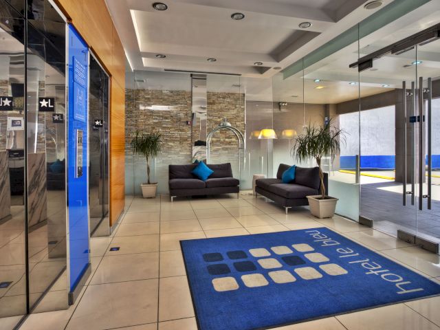 A hotel lobby with a blue rug, two gray sofas, and a glass wall.
