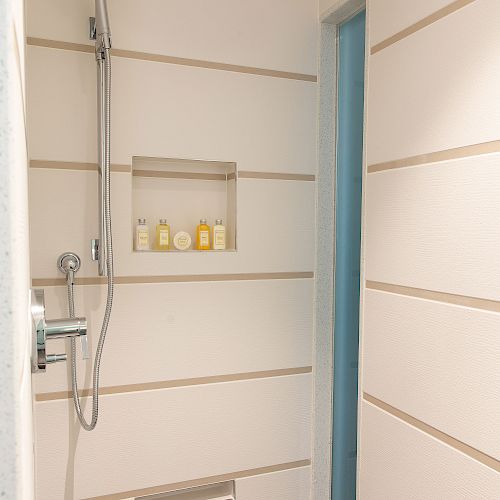 A modern shower area with a built-in shower head, a shelf holding toiletries, and sleek horizontal paneling on the walls.