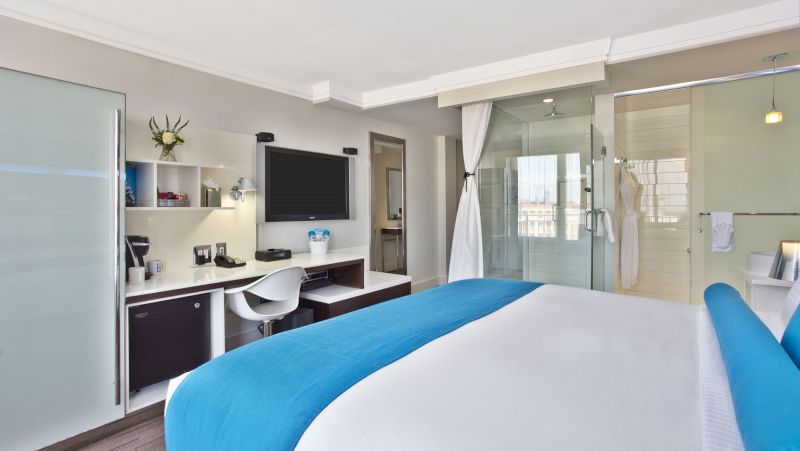 A hotel room with a king-sized bed, desk, TV, and shower
