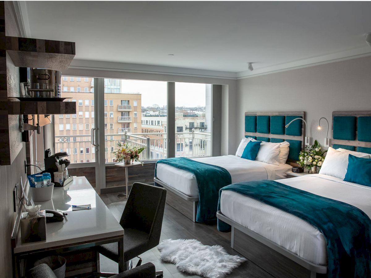 The image features a modern hotel room with two beds, a desk, city view through large windows, and elegant decor.