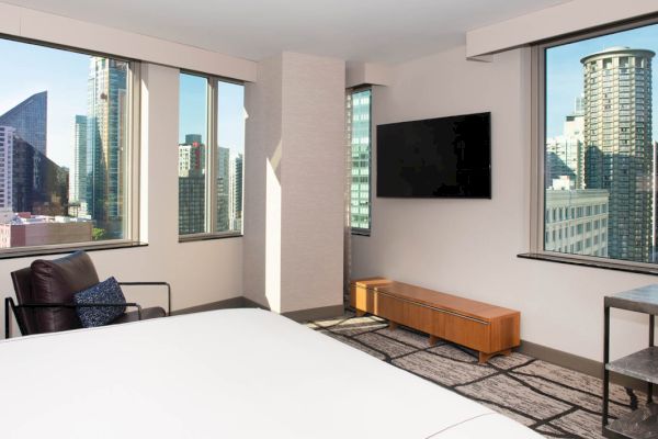 A hotel room with a city view, a bed, chair, TV, and wooden furniture.