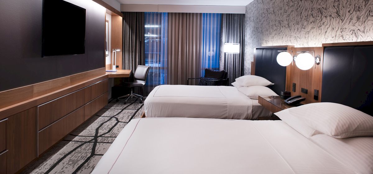 A hotel room with two beds, a desk, and a TV.
