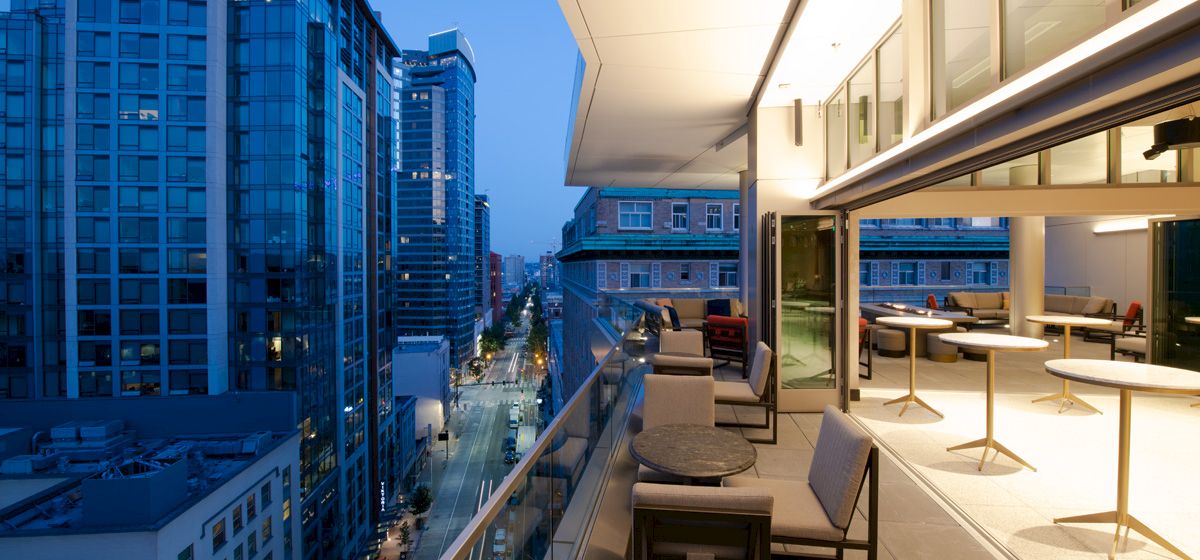 A balcony with outdoor seating and a city view at dusk.