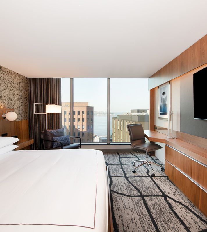 A wide view of a hotel room with a bed, desk, chair, and TV