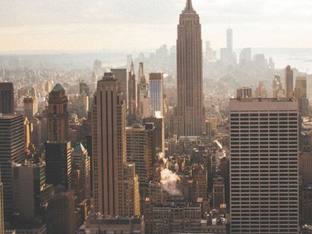 A cityscape featuring numerous skyscrapers under a slightly overcast sky, with a tall iconic building prominently standing in the distance.